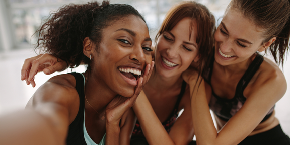 3 women in sports wear laughing and leaning on eachother