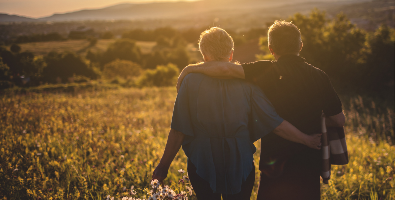 Couple with arms around each other walking toward sunset