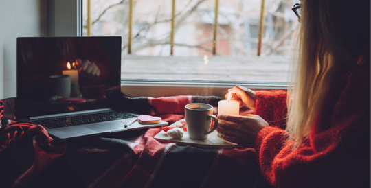 Women in cosy setting lighting a candle and looking at her computer