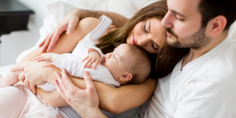 mother, father and baby lying in bed