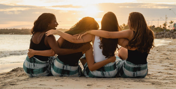 4 women on a beach watching the sunset with their arms across each others back